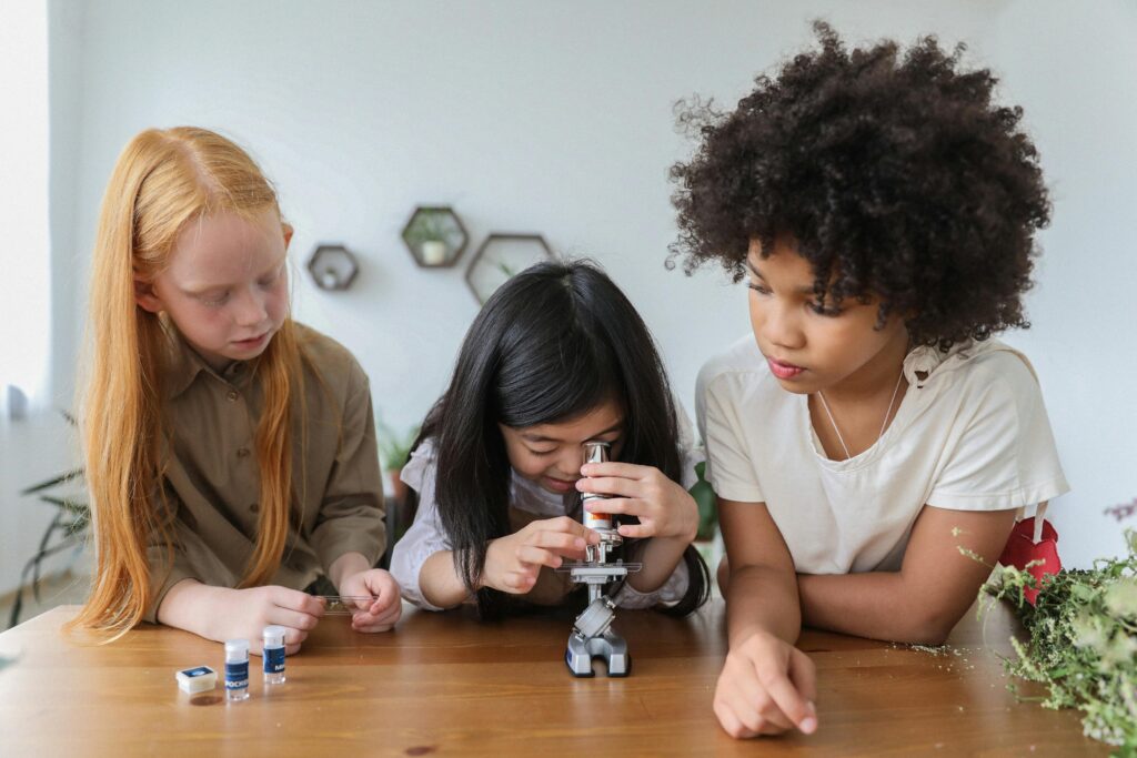 Concentrated multiethnic children in casual clothes watching in microscope while studying together