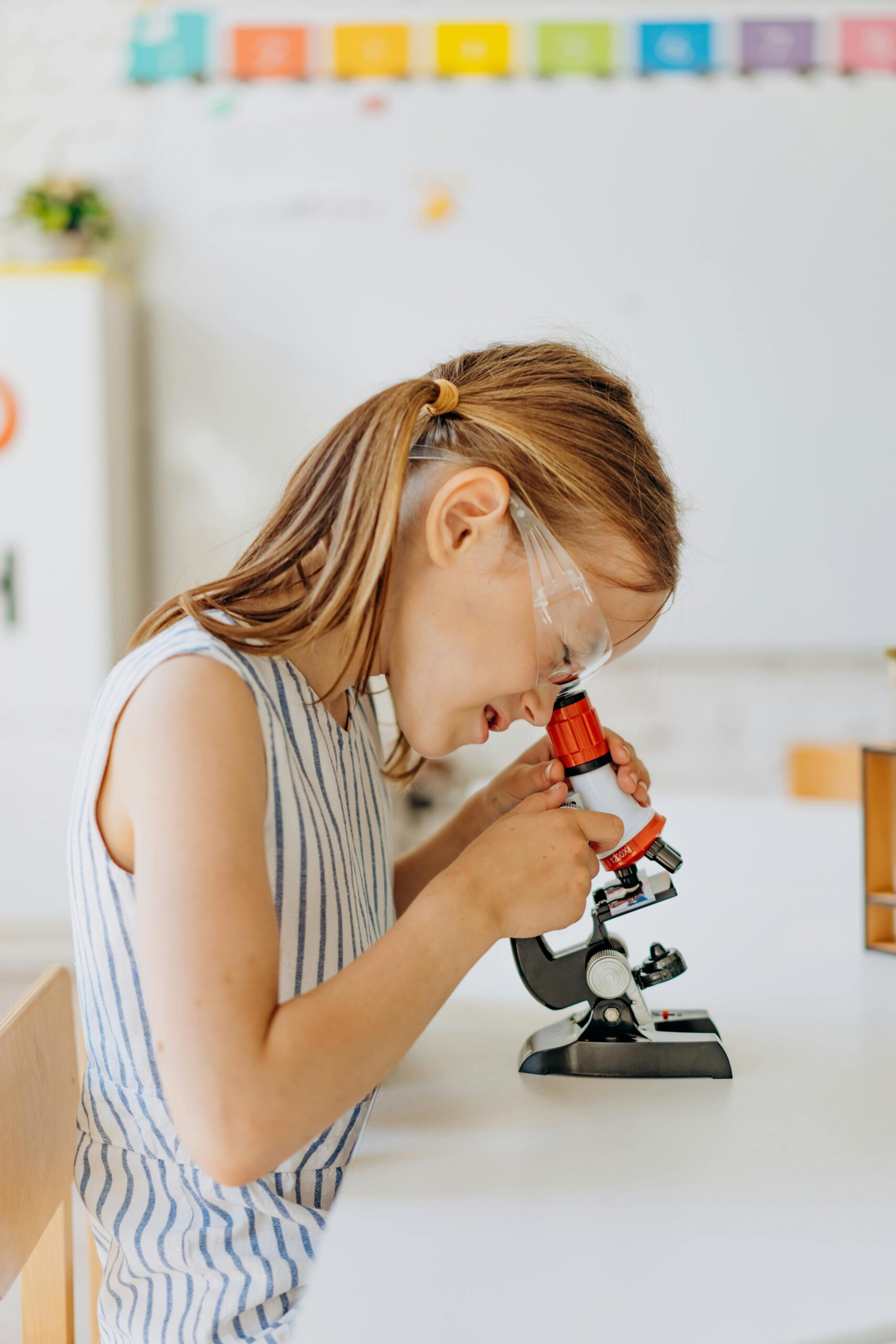 A young girl exploring science education using a microscope indoors, showcasing curiosity and learning.